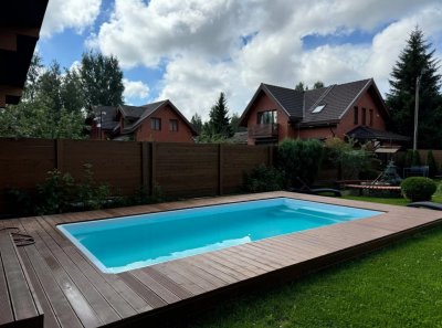 Прямоугольный бассейн с террасной доской и зелёным газоном во дворе
